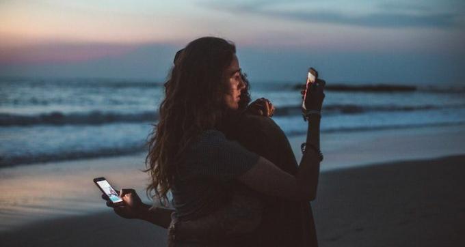 Et par krammer og kigger på deres telefoner på stranden