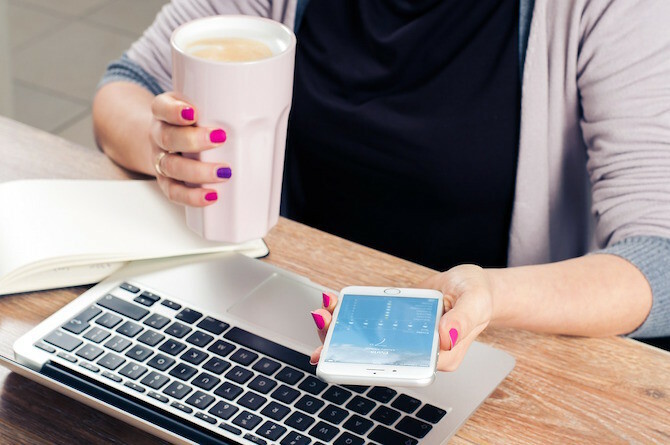 Kvinde, der drikker kaffe på telefon og Mac