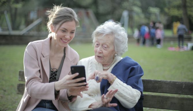 En ung kvinde og en gammel kvinde ser på en telefon på bænken
