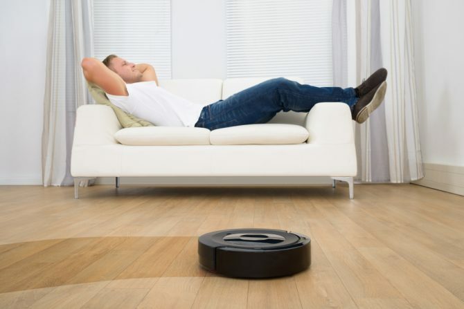 Mand slapper af i sofaen med robotstøvsuger på trægulv