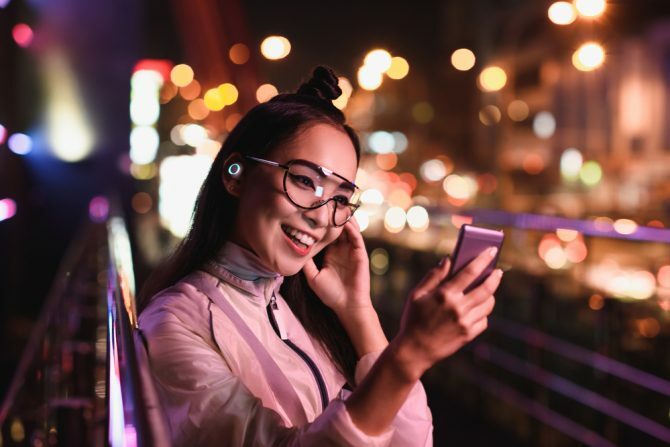 glad asiatisk pige, der har videochat ved hjælp af smartphone og i ørehovedtelefoner